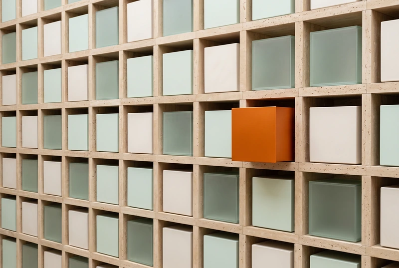 A travertine storage wall of neatly fitted boxes with one orange box pulled forward